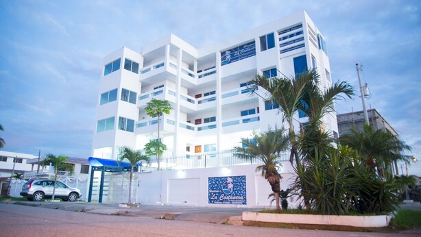 Un hotel de varios pisos con fachada blanca, balcones y palmeras en primer plano.