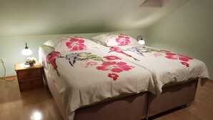 Ein Doppelbett mit floraler Bettwäsche, Nachttischlampen und einem Nachttisch mit Pflanze.