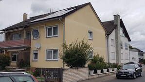 Ein zweistöckiges Wohngebäude mit gelber Fassade, mehreren Fenstern und einer Satellitenschüssel.