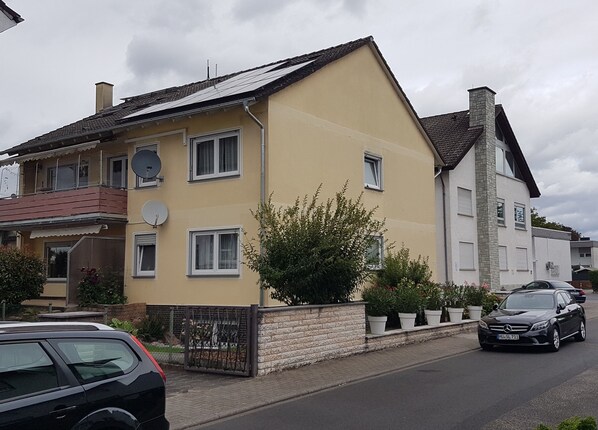 Un edifici residencial de dues plantes amb façana groga, nombroses finestres i una antena satèl·lit.