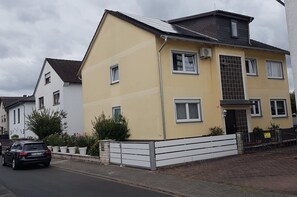 Un edifici residencial de dues plantes amb façana groga, adorns blancs i teulada metàl·lica.