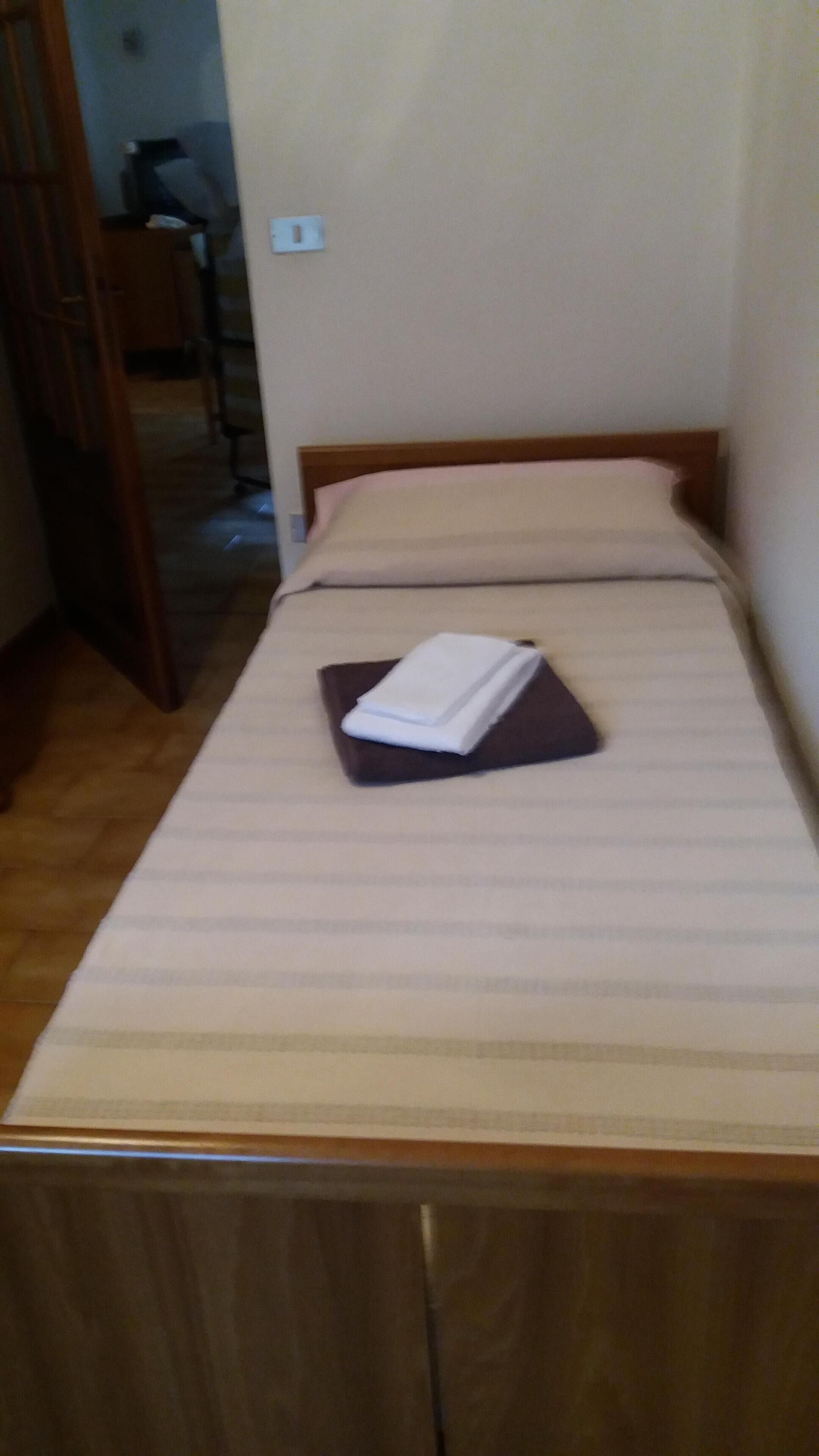Ein Einzelbett mit Holz-Kopfteil und weißem Matratzenbezug.