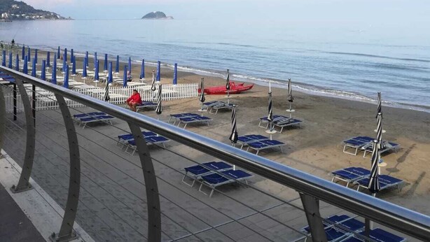 Una playa con tumbonas y sombrillas azules, un muelle de madera y una isla a lo lejos.