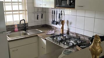 Uma cozinha com armários brancos, pia de aço inoxidável, fogão a gás e micro-ondas.