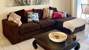A living room with a brown sectional sofa, a coffee table with a bowl, and a large elephant painting on the wall.