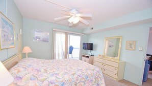 Une chambre à coucher comprenant un lit, une commode, un téléviseur et un ventilateur de plafond.