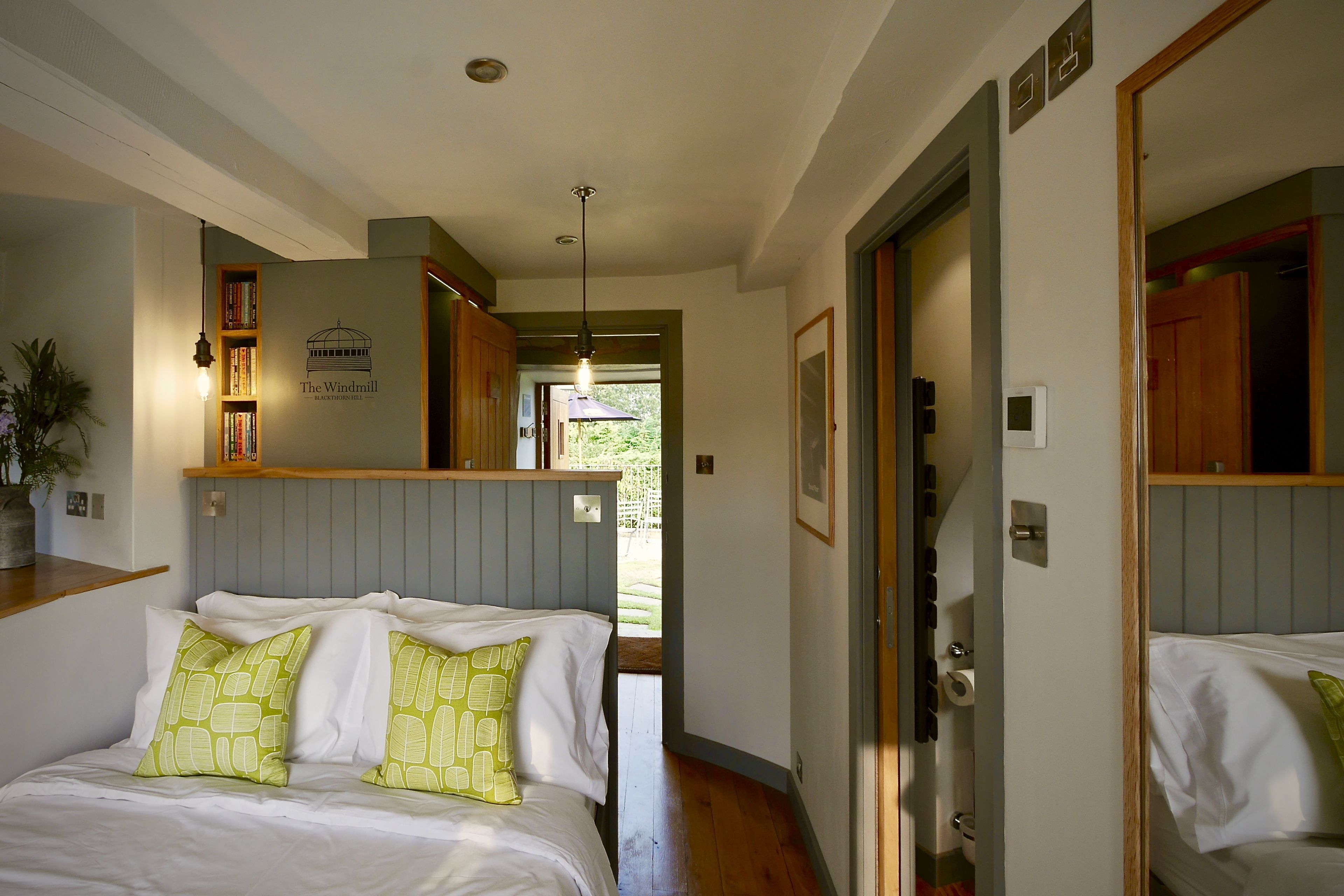 A bedroom with a bed, pillows, a nightstand, a bookshelf, and a door leading to another room.