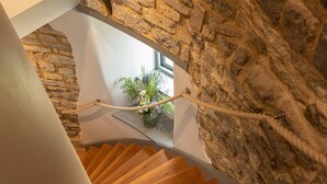 Una escalera en espiral de madera con baranda de cuerda, que conduce a una habitación con pared de piedra y una ventana con una planta.