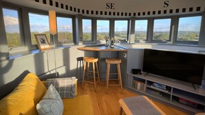 Una sala moderna con un televisor grande, taburetes de madera, un sofá y una zona de bar.