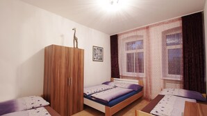 A bedroom with two single beds, a wooden wardrobe, a window with curtains, and a ceiling light.