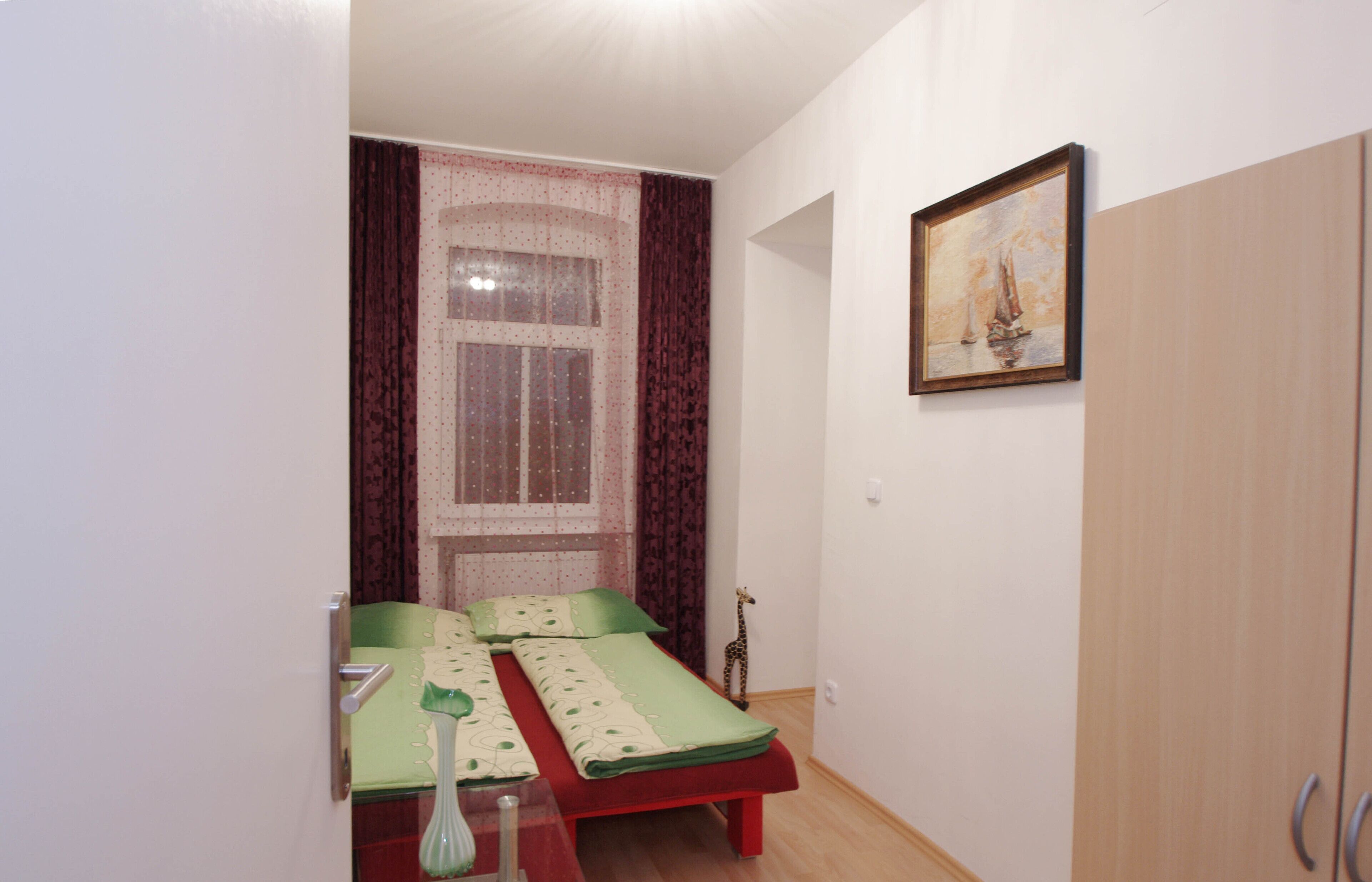 Una habitación pequeña con dos camas individuales, una ventana con cortinas, un cuadro en la pared y un armario.