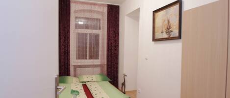 Una habitación pequeña con dos camas individuales, una ventana con cortinas, un cuadro en la pared y un armario.