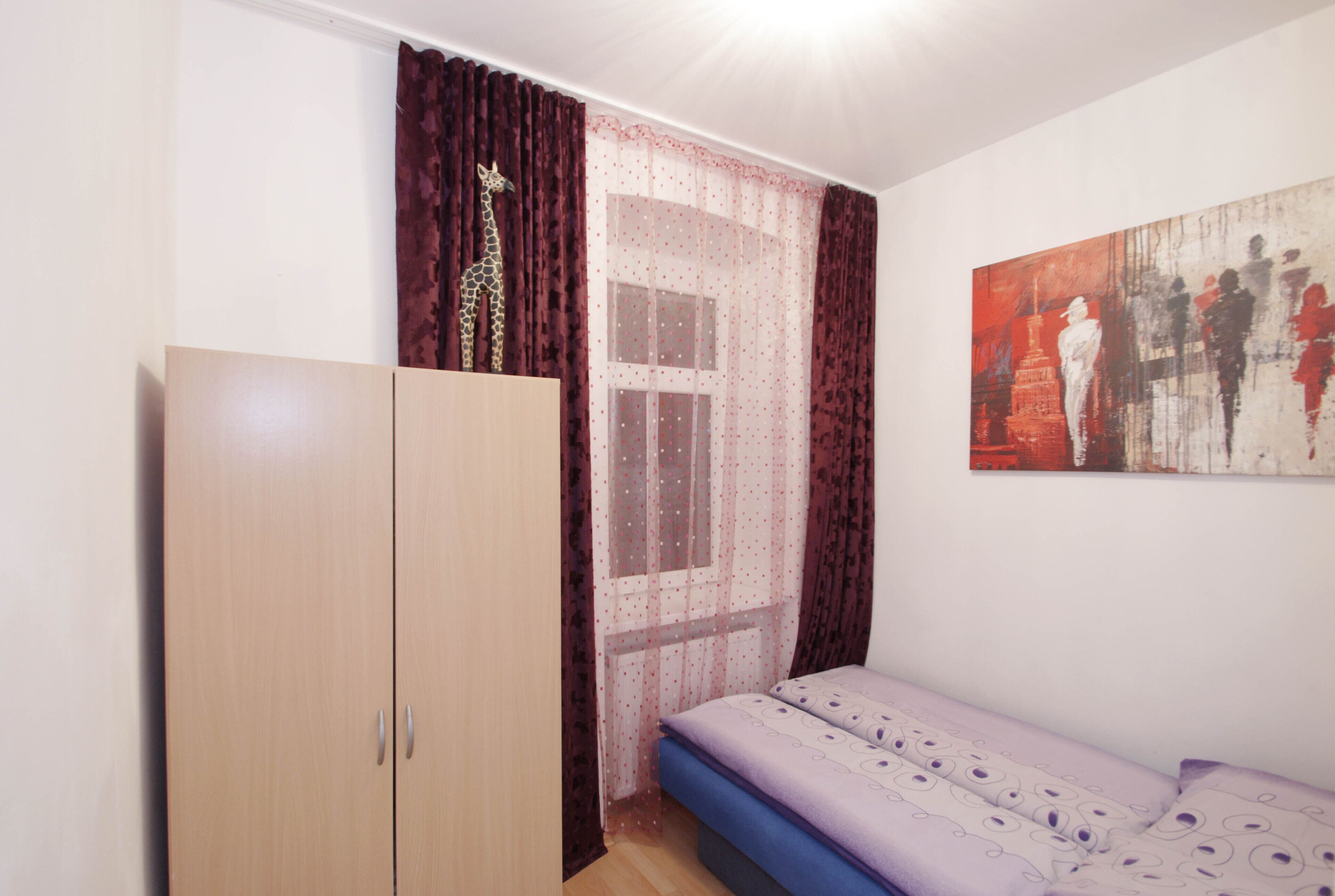 Una camera da letto con un letto, un armadio, una finestra con tende e un quadro appeso al muro.