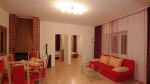 A living room with a red sofa, a dining table with chairs, a fireplace, and a hallway leading to another room.