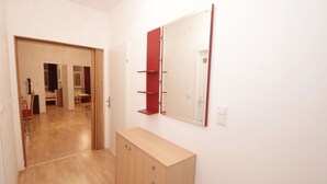 A room with a wooden floor, a wooden cabinet, a mirror, and a door leading to another room.