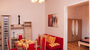 A compact living space with a dining area, a red sofa, a wooden wardrobe, and a painting on the wall. - Raisa Superior Apartment with 2 bedrooms, 2 terraces and marble bathroom  (Pressbaum)