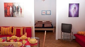 A room with a bed, a TV, and a dining area with a table set for two. - Raisa Superior Apartment with 2 bedrooms, 2 terraces and marble bathroom  (Pressbaum)