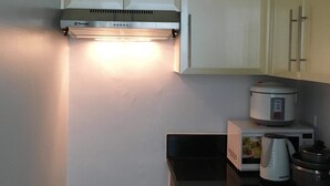 Une cuisine avec des meubles blancs, une hotte de cuisinière en acier inoxydable, un four à micro-ondes, une bouilloire et un cuiseur à mijoter.