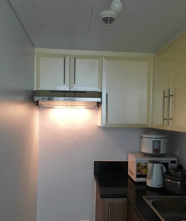 A kitchen with white cabinets, a stainless steel range hood, a microwave, a kettle, and a slow cooker. - CF10C The Parkside Villas, Family room with kichen, dining,living area & balcony (Pasay)