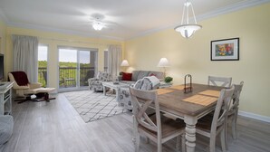 A spacious living room with a balcony, a dining area with a wooden table, and a seating arrangement including a sofa and chairs. - Rate Reduced! Tops'l Condo -  Walk to Beach, Tropical Pool, Balcony. (Miramar Beach)
