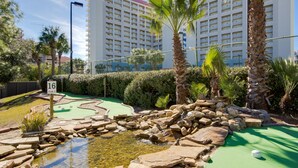 A golf course with a water feature, palm trees, and a hedge. - Rate Reduced! Tops'l Condo -  Walk to Beach, Tropical Pool, Balcony. (Miramar Beach)