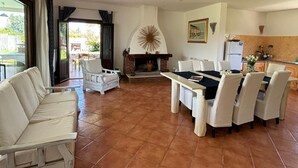 Un amplio salón con chimenea, muebles blancos y vistas a través de grandes ventanales.