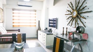 A modern living room with a sofa, a coffee table, a TV, and a decorative sun-like wall piece. - Eastwood City Secured w/ Panoramic View (Quezon City)