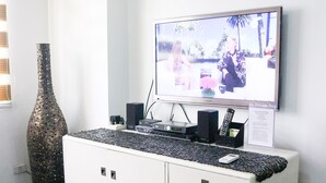A living room with a flat-screen TV mounted on the wall, a white entertainment unit with drawers, a large decorative vase, and a remote control stand. - Eastwood City Secured w/ Panoramic View (Quezon City)