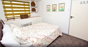 Quarto principal com cama de casal, janela com persianas, radiador e porta com puxador.