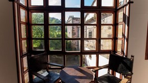 Una habitación con un amplio ventanal, dos sillas de madera y una mesita.