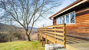 A wooden cabin with a deck and stone steps, surrounded by a grassy area and trees.