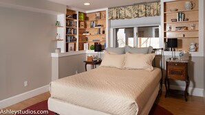 A bedroom with a large bed, built-in bookshelves, a bedside table, and a window with curtains.