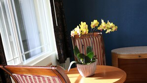 A dining area with a round wooden table, two chairs with striped upholstery, and a potted plant with yellow flowers. - Valli Hi Motel (San Ysidro)