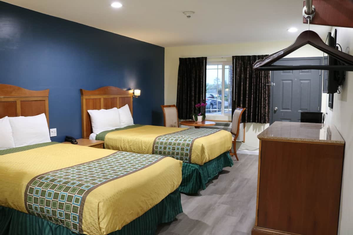A hotel room with two beds, a desk, a chair, and a wardrobe.