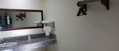 A bathroom with a granite countertop sink, a mirror, a towel rack, and a towel dispenser.