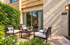 A patio with outdoor furniture, a potted plant, and a building with a textured wall and a number sign.