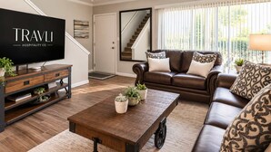 A living room with a television, leather sofa, coffee table, and a staircase. - Walk to Old Town | 2 King Beds + 4 Heated Pools (Scottsdale)