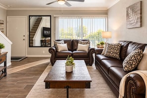 A living room with a brown leather sofa, a wooden coffee table, and a large window with blinds. - Walk to Old Town | 2 King Beds + 4 Heated Pools (Scottsdale)