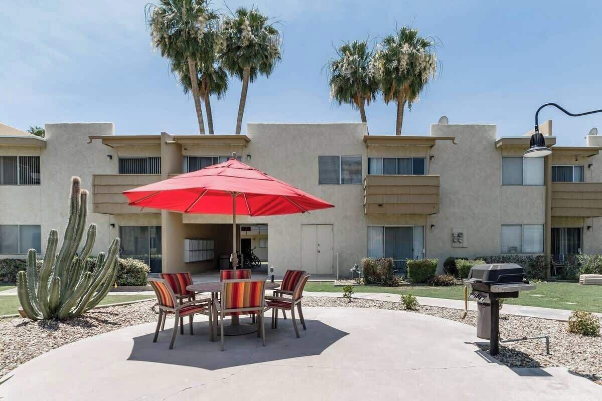 Un patio con una sombrilla roja, mobiliario exterior, un cactus y una parrilla.