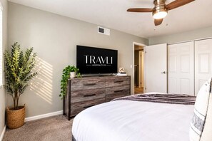 A bedroom with a bed, a dresser, a flat-screen TV, a ceiling fan, and a door.