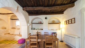 Un comedor rústico con suelo de piedra, mesa y sillas de madera. Se observan arcos con repisas sobre la mesa.