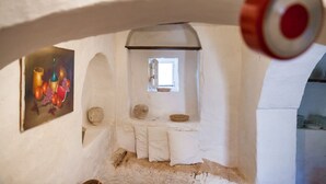 Un interior rústico con una pequeña ventana, un cuadro en la pared y un banco blanco.