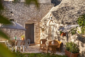 A stone building with a rustic exterior, outdoor seating area with white plastic chairs and wicker tables, and a potted plant. - Relaxing Trullo -
Original and comfortable trullo in Valle d'Itria Puglia (Locorotondo, Bari)