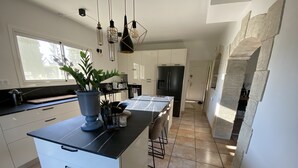 Une cuisine moderne avec des meubles blancs, un plan de travail noir et un îlot central. Des luminaires suspendus et une plante en pot ornent l’îlot.