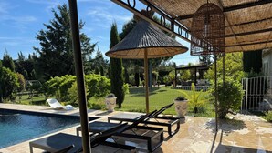 Un espace aménagé au bord de la piscine, avec des chaises longues, une pergola et une vue sur un jardin paysager.
