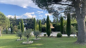 Un jardin bien entretenu, avec une pelouse soigneusement taillée, divers arbres et un chemin en pierre.