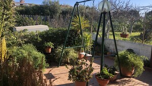 Un jardín con diversas plantas en macetas, un columpio y un cielo azul despejado.