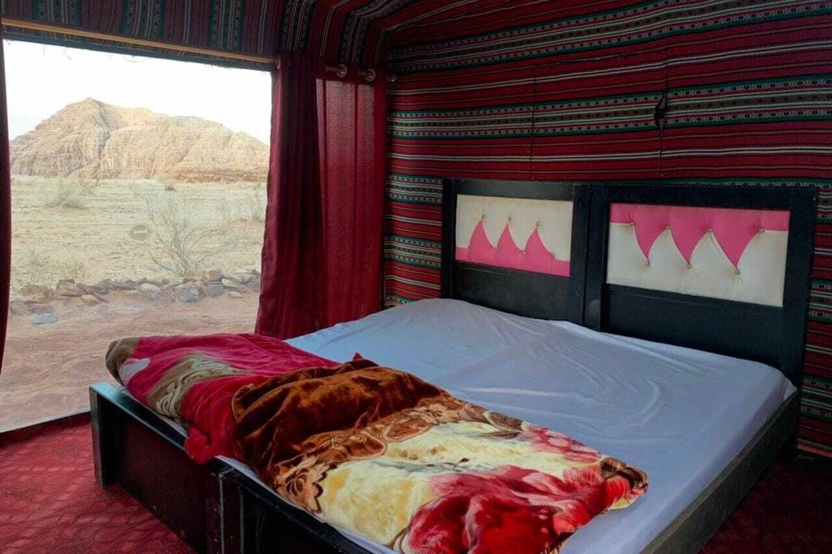A bed with a red and beige blanket, a window with a view of a desert landscape, and striped wallpaper.