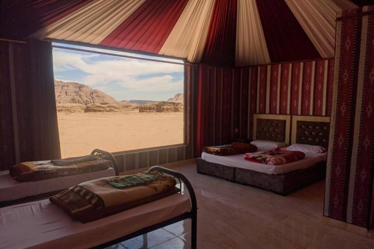 A room with a large window, two beds, and a view of a desert landscape.