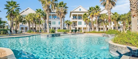 A swimming pool surrounded by palm trees and multi-story buildings with balconies.
